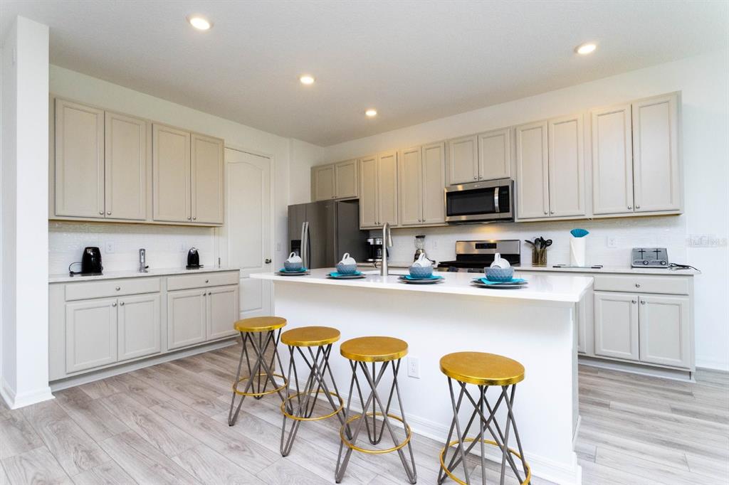 A kitchen with light-colored cabinets, a white island, four bar stools, and wood-look flooring — 624 BENOI DRIVE, DAVENPORT, FL