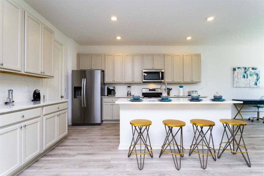 A kitchen features light-colored cabinetry, stainless steel appliances, a white island, and four gold stools — 624 BENOI DRIVE, DAVENPORT, FL