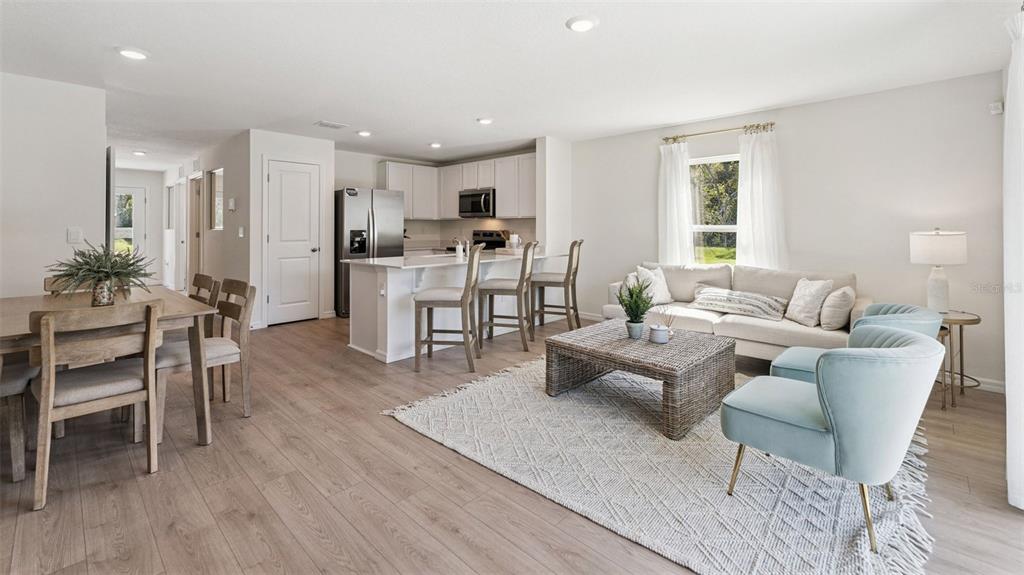 An open-concept living room and kitchen feature light wood floors, white cabinetry, and neutral furniture — 793 PRESTON COVE DRIVE, ST CLOUD, FL