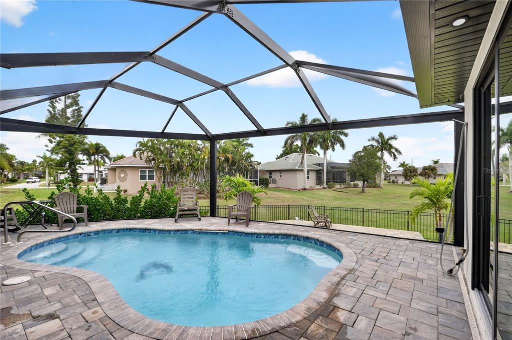 A screened-in patio features a kidney-shaped swimming pool and stone pavers overlooking a grassy yard — 609 MONACO DRIVE, PUNTA GORDA, FL