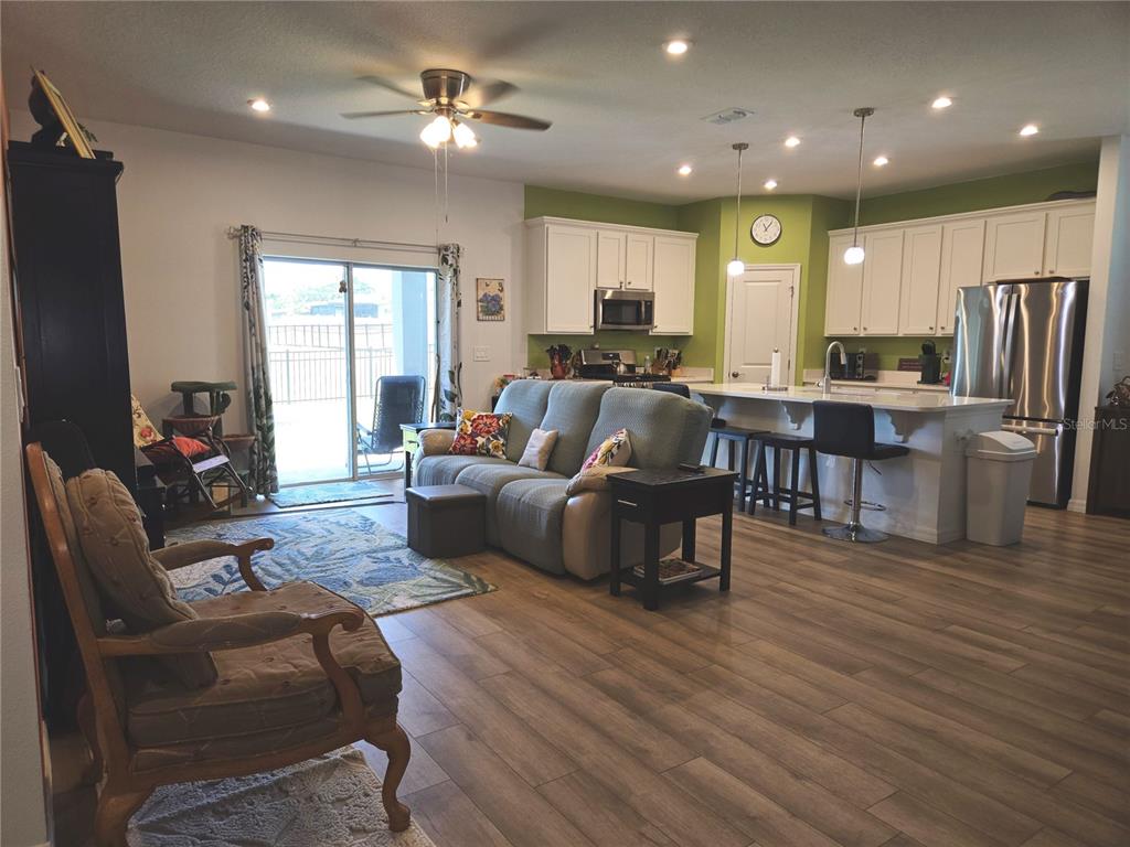 An open-concept living room and kitchen with wood-look flooring, white cabinetry, and a sliding door — 3995 CAYMAN DRIVE, TITUSVILLE, FL