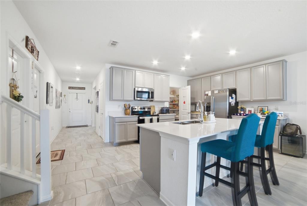 A kitchen features light gray cabinets, a white island with blue stools, and tiled floors — 4980 FOUR STRAND COURT, ST CLOUD, FL