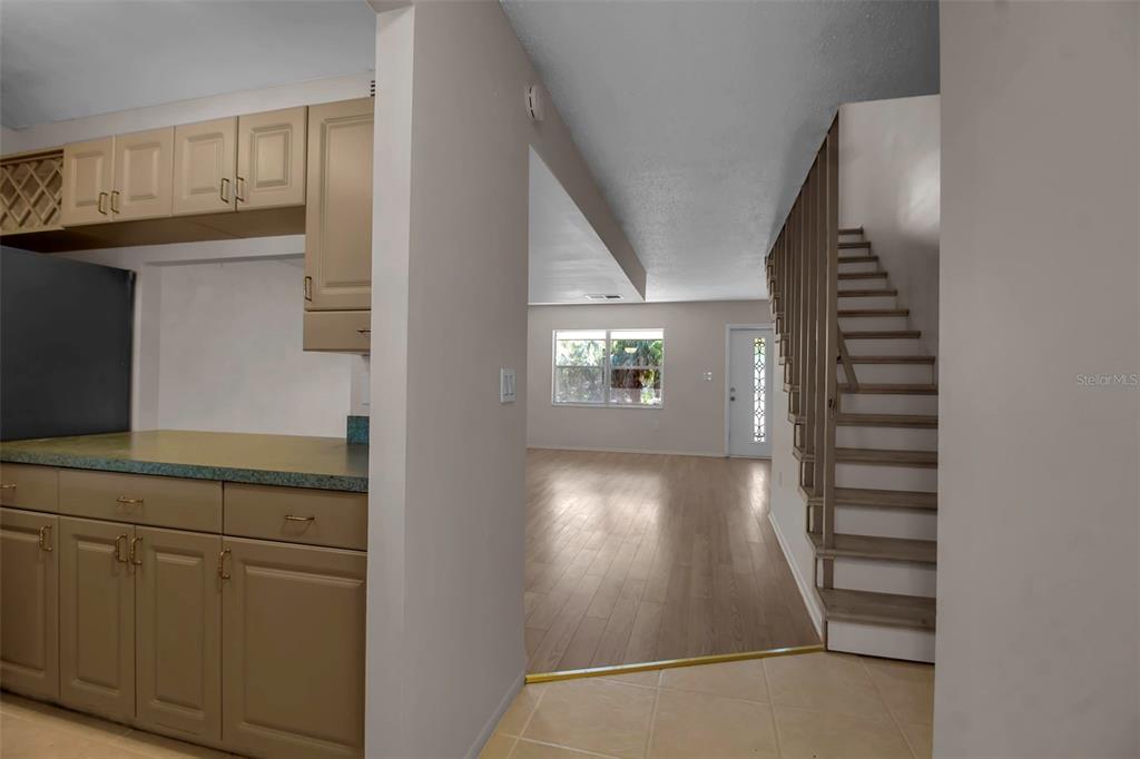 A kitchen with tan cabinets overlooks a living area with wood floors and a staircase — 3212 RAMBLEWOOD DRIVE N UNIT 3212, SARASOTA, FL