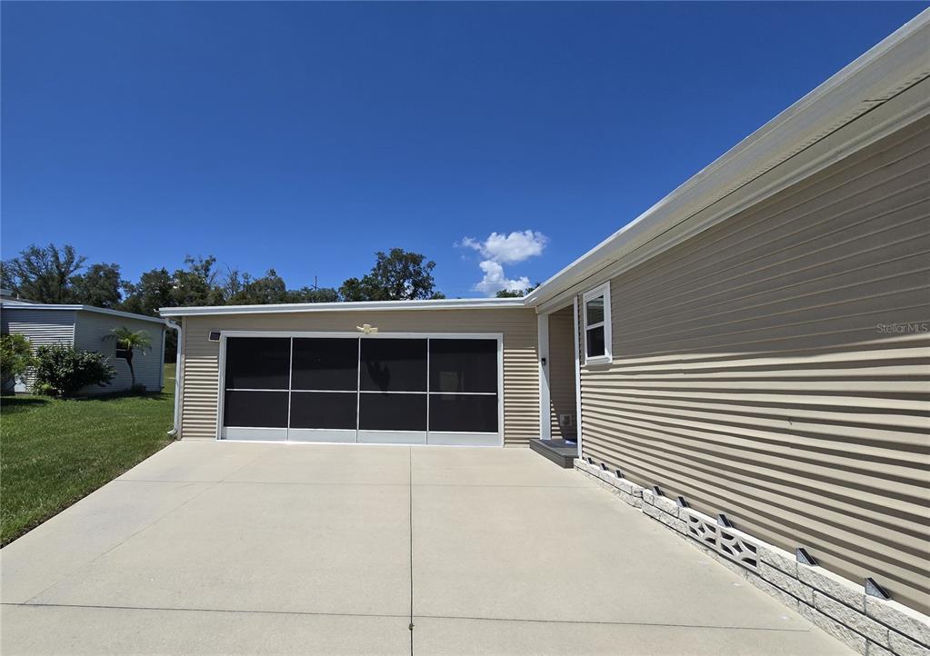 A beige house exterior features a screened-in garage and a concrete driveway under a blue sky — 4139 GREENBLUFF COURT UNIT 795, ZELLWOOD, FL