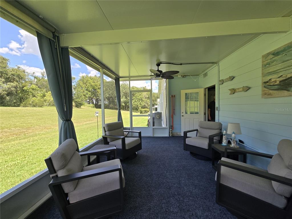 A screened-in porch features four armchairs, a ceiling fan, and a view of a grassy yard — 4139 GREENBLUFF COURT UNIT 795, ZELLWOOD, FL