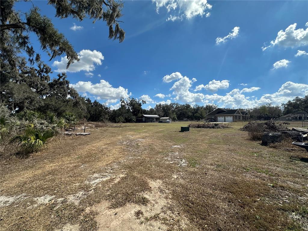 A wide, grassy lot features scattered debris, a small shed, and a house in the distance — 9988 BRYANT ROAD, LITHIA, FL
