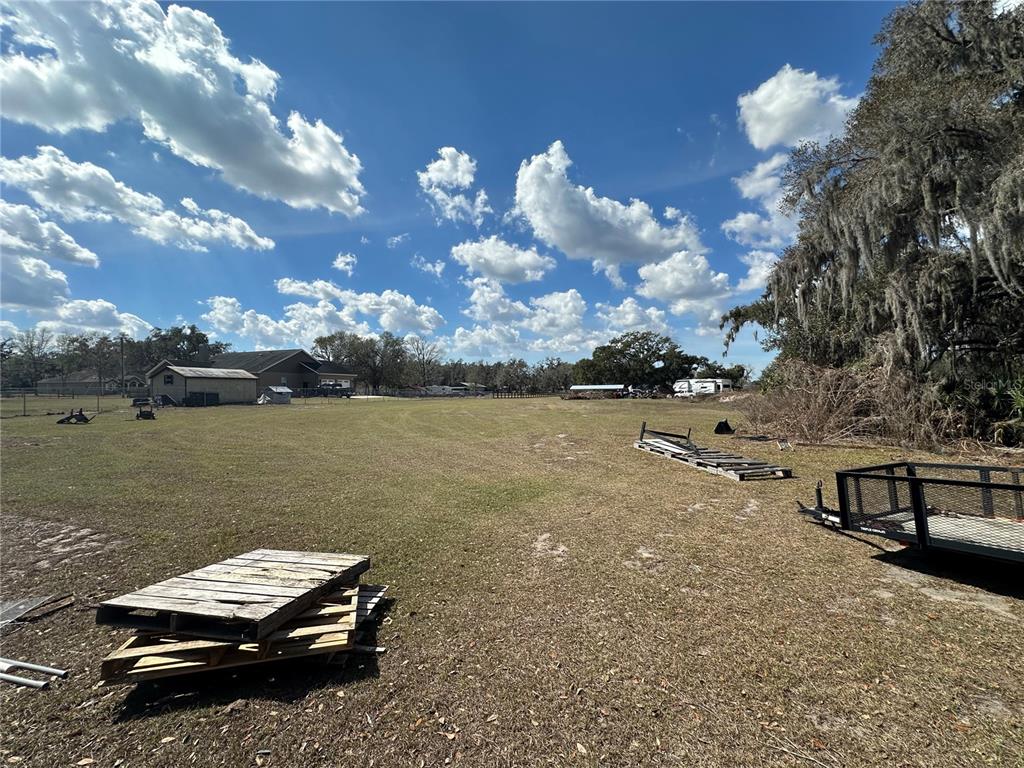 A large, grassy, open lot features scattered wooden pallets and a trailer under a blue sky — 9988 BRYANT ROAD, LITHIA, FL