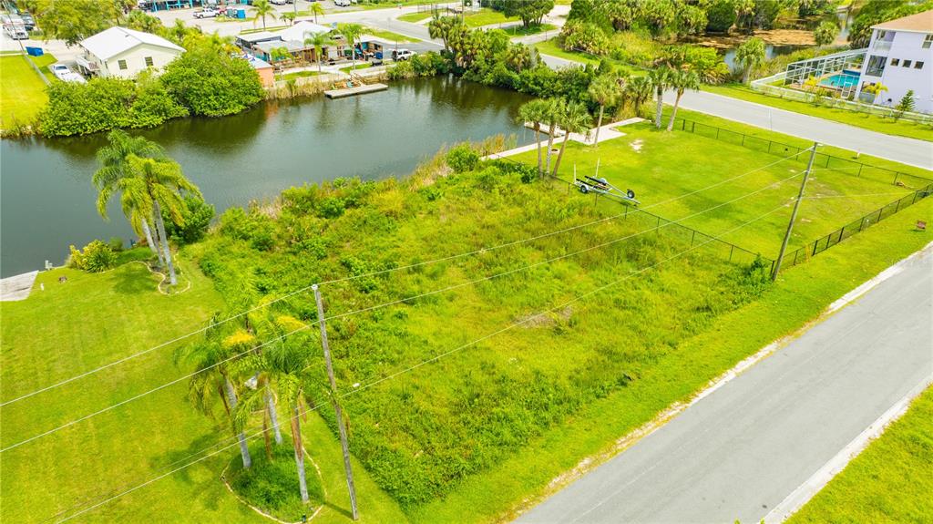 An aerial view shows a vacant, grassy waterfront lot bordered by a road and canal — 3326 FERNLEAF DRIVE, HERNANDO BEACH, FL