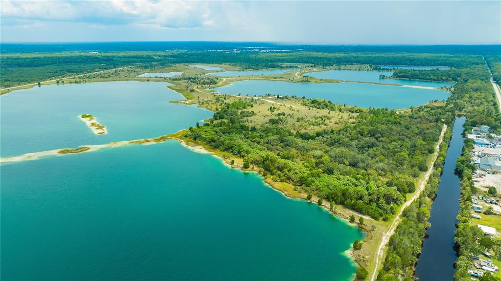 An aerial view shows a large turquoise lake with a small island and surrounding forest — 3326 FERNLEAF DRIVE, HERNANDO BEACH, FL