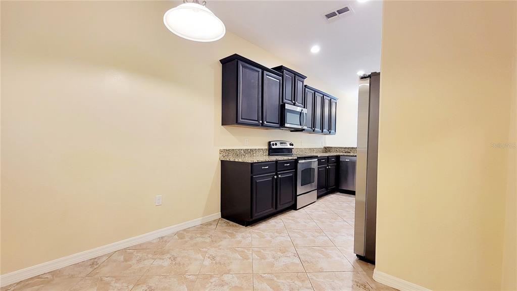 A kitchen features dark wood cabinets, granite countertops, stainless steel appliances, and tiled flooring — 9540 TRUMPET VINE LOOP, TRINITY, FL
