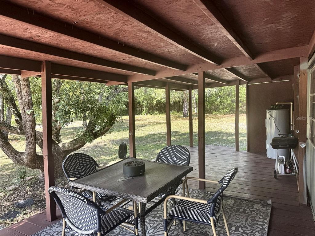 A covered wooden deck features a dining set, a grill, and a water heater — 6838 N CARL G ROSE HIGHWAY, HERNANDO, FL