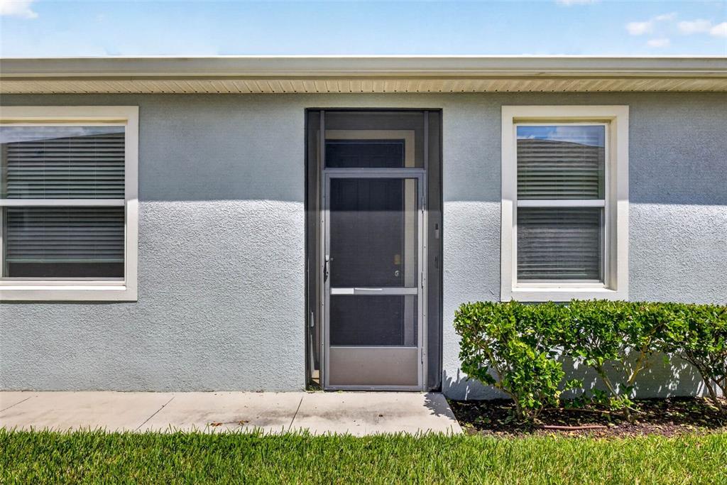 The exterior of a house features a screen door, two windows, and a small hedge — 7460 STONEBROOK CIRCLE, WESLEY CHAPEL, FL