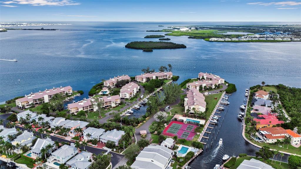 An aerial view shows a waterfront residential complex with boat docks, a pool, and tennis courts — 3840 MARINERS WAY UNIT 514A, CORTEZ, FL