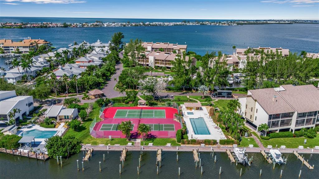 An aerial view shows a waterfront residential complex with tennis courts, a pool, and docks — 3840 MARINERS WAY UNIT 514A, CORTEZ, FL