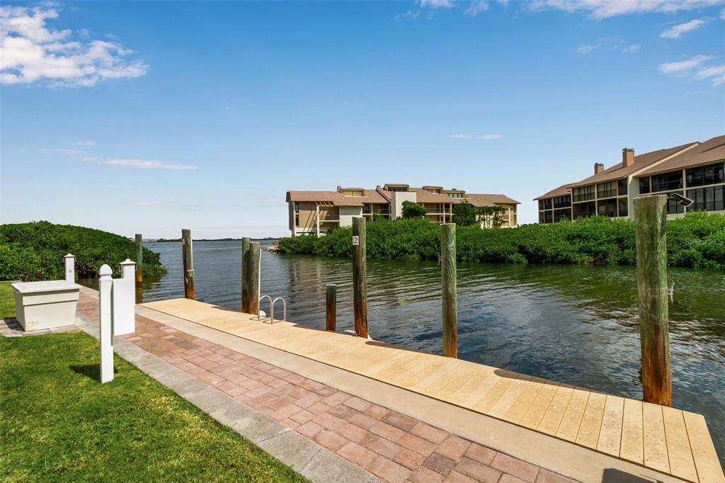 A wooden boat dock extends into a canal with multi-story residential buildings in the background — 3840 MARINERS WAY UNIT 514A, CORTEZ, FL