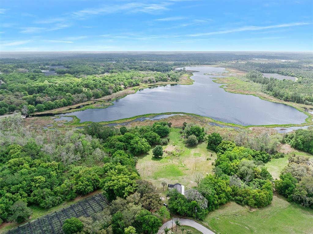An aerial view shows a house situated on a grassy lot bordering a large lake — 141 N PINE STREET, PIERSON, FL