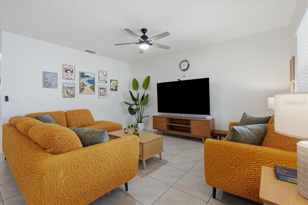 A living room features yellow textured sofas, a wooden media console, and a ceiling fan — 1113 GRIFFON AVE, LAKE ALFRED, FL