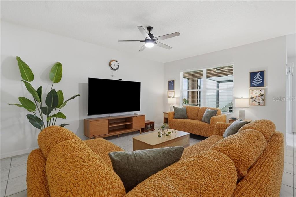 A living room features textured mustard-colored sofas, a wooden media console, and a ceiling fan — 1113 GRIFFON AVE, LAKE ALFRED, FL