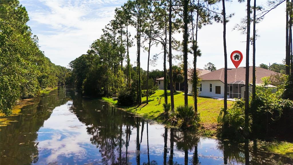 A white house with a screened porch sits beside a canal surrounded by tall trees — 64 WHITTINGTON DRIVE, PALM COAST, FL
