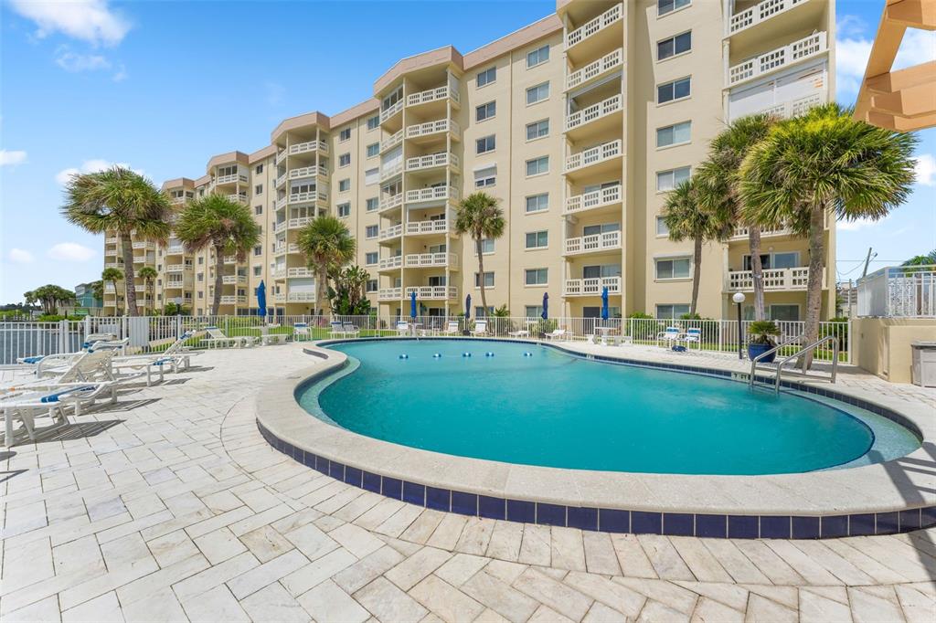 A swimming pool sits on a paved patio in front of a multi-story apartment building — 3606 S PENINSULA DRIVE UNIT 103, PORT ORANGE, FL