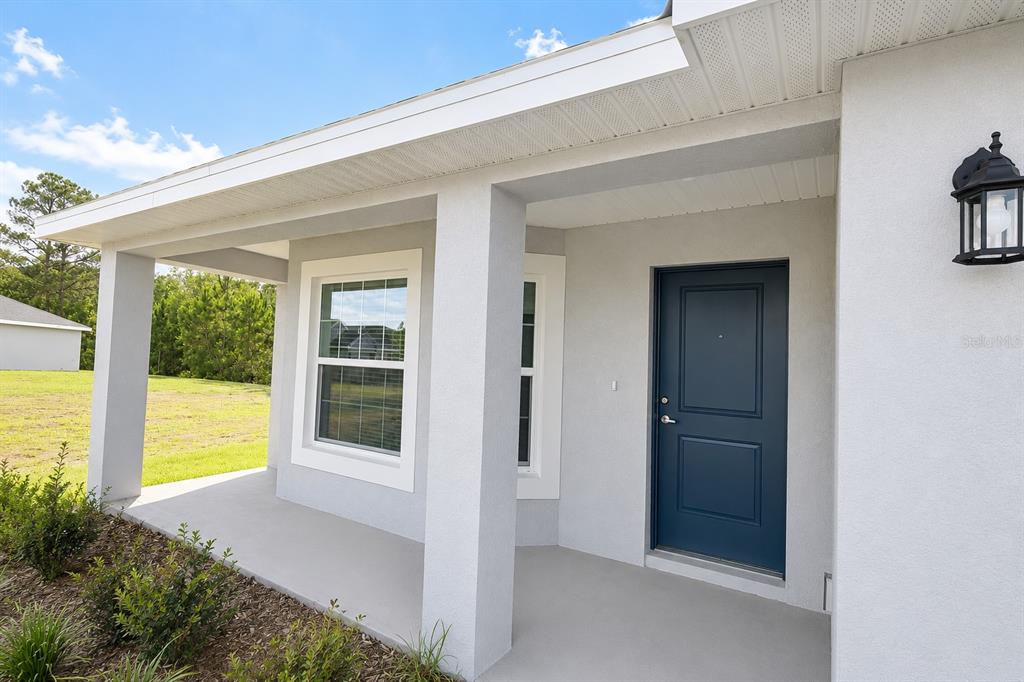 A covered front porch with a blue door and white stucco exterior walls — 7606 BENT TREE LOOP, ST CLOUD, FL