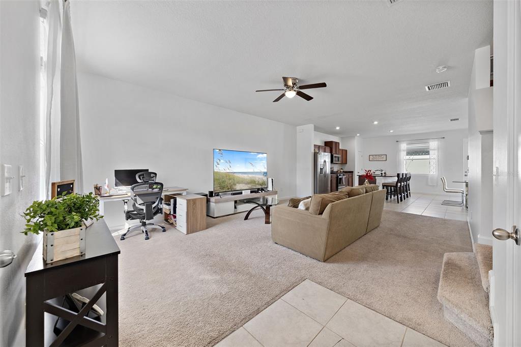 An open-concept living room features a desk area, a sofa, and a kitchen in the background — 14929 PROMENADE PARKWAY, ODESSA, FL