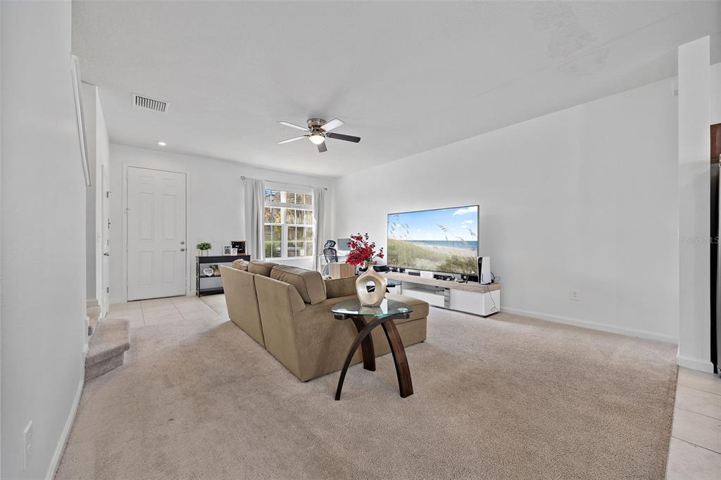 A living room features beige carpeting, a tan sectional sofa, a television, and a ceiling fan — 14929 PROMENADE PARKWAY, ODESSA, FL