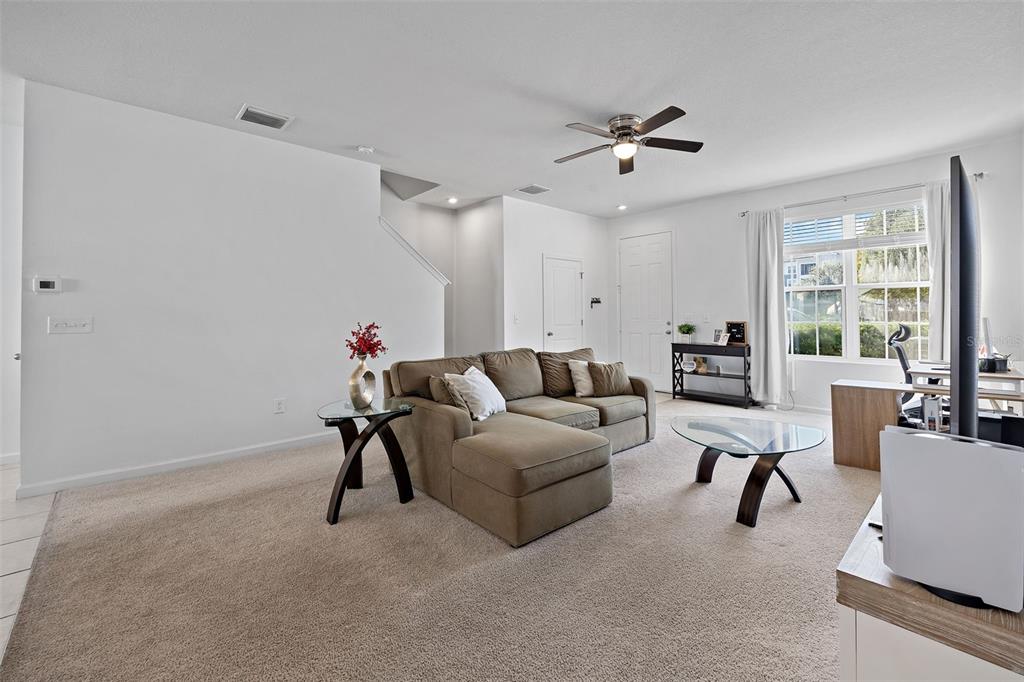 A living room with beige carpet, a brown sectional sofa, and a glass coffee table — 14929 PROMENADE PARKWAY, ODESSA, FL