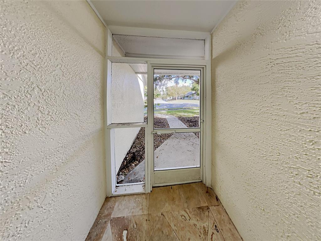 A covered entryway features textured walls, a screen door, and unfinished subflooring — 1320 NOELL BOULEVARD, PALM HARBOR, FL