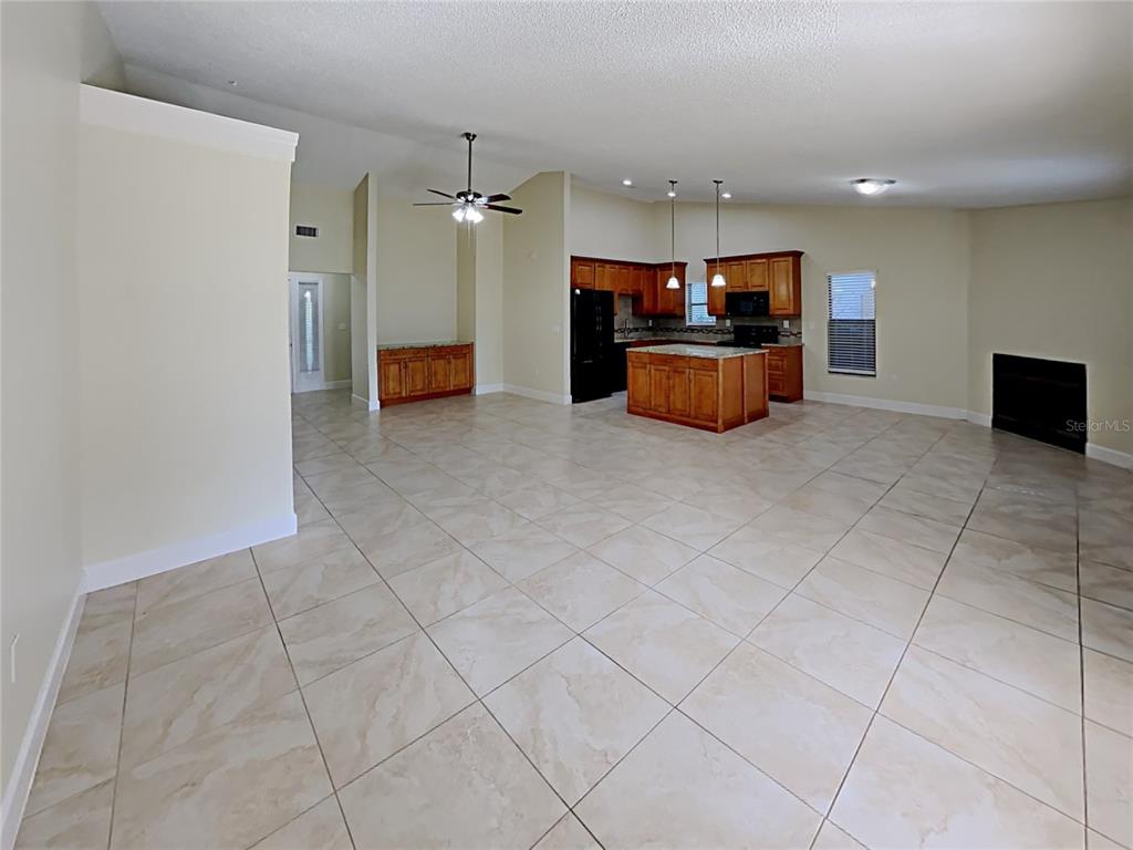 An open-concept living area features tile flooring, a kitchen with wood cabinets, and a fireplace — 1320 NOELL BOULEVARD, PALM HARBOR, FL