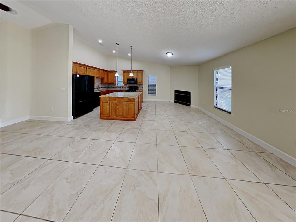 An open-concept kitchen with wood cabinets and a granite island overlooks a tiled living area — 1320 NOELL BOULEVARD, PALM HARBOR, FL