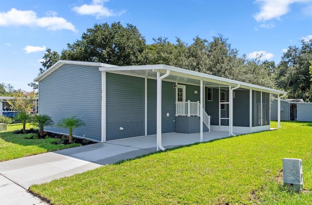 A blue-sided manufactured home features a covered carport and a screened-in porch area — 25124 HUCKLEBERRY WAY, ASTATULA, FL