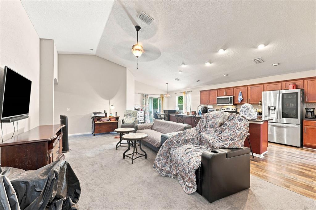 A living room with gray carpet flows into an open kitchen with wood cabinets — 322 WOODS LANDING DRIVE, LADY LAKE, FL