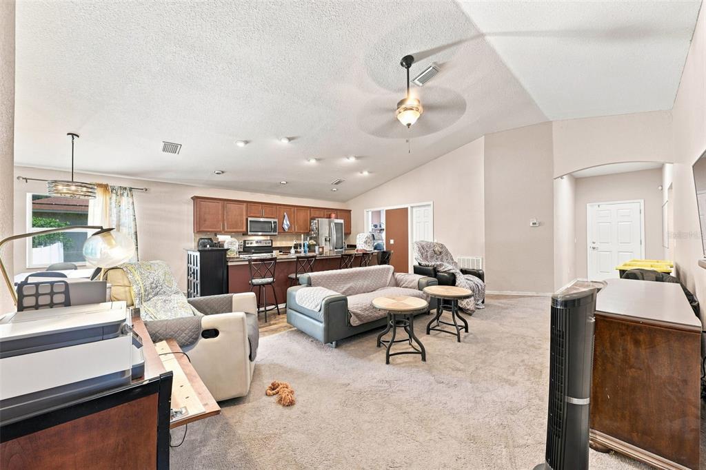 A living room with carpeted floors opens to a kitchen featuring wood cabinets and bar seating — 322 WOODS LANDING DRIVE, LADY LAKE, FL
