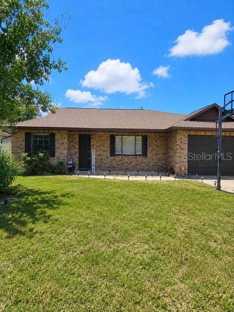 A single-story brick house with a dark roof, garage, and front lawn under a blue sky — 619 N FIRWOOD DRIVE, DELTONA, FL