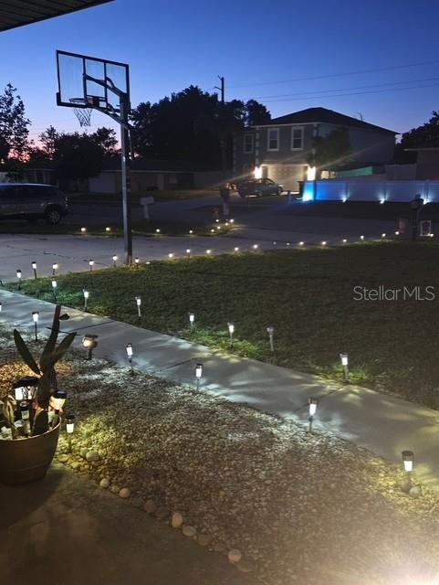A residential driveway and front lawn are illuminated by numerous small solar path lights at dusk — 619 N FIRWOOD DRIVE, DELTONA, FL