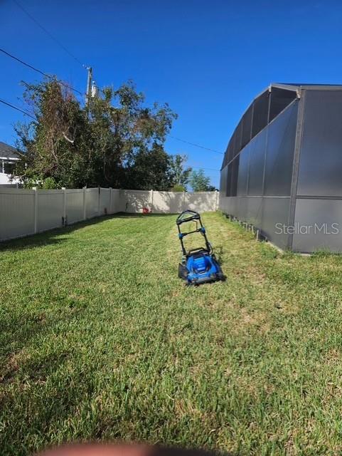 A blue lawnmower sits in the grass of a backyard enclosed by a white fence — 619 N FIRWOOD DRIVE, DELTONA, FL
