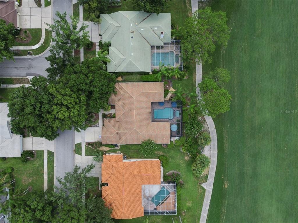 An aerial view shows three houses with swimming pools and tiled roofs bordering a golf course — 17714 GREY EAGLE ROAD, TAMPA, FL