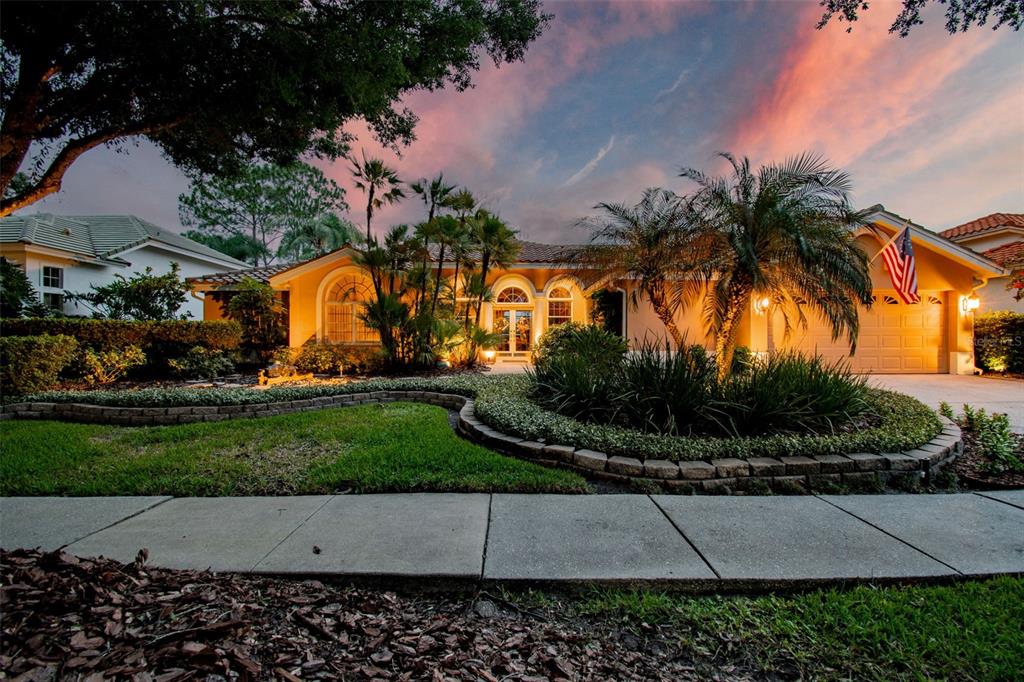 A single-story house with a landscaped front yard and an American flag at sunset — 17714 GREY EAGLE ROAD, TAMPA, FL