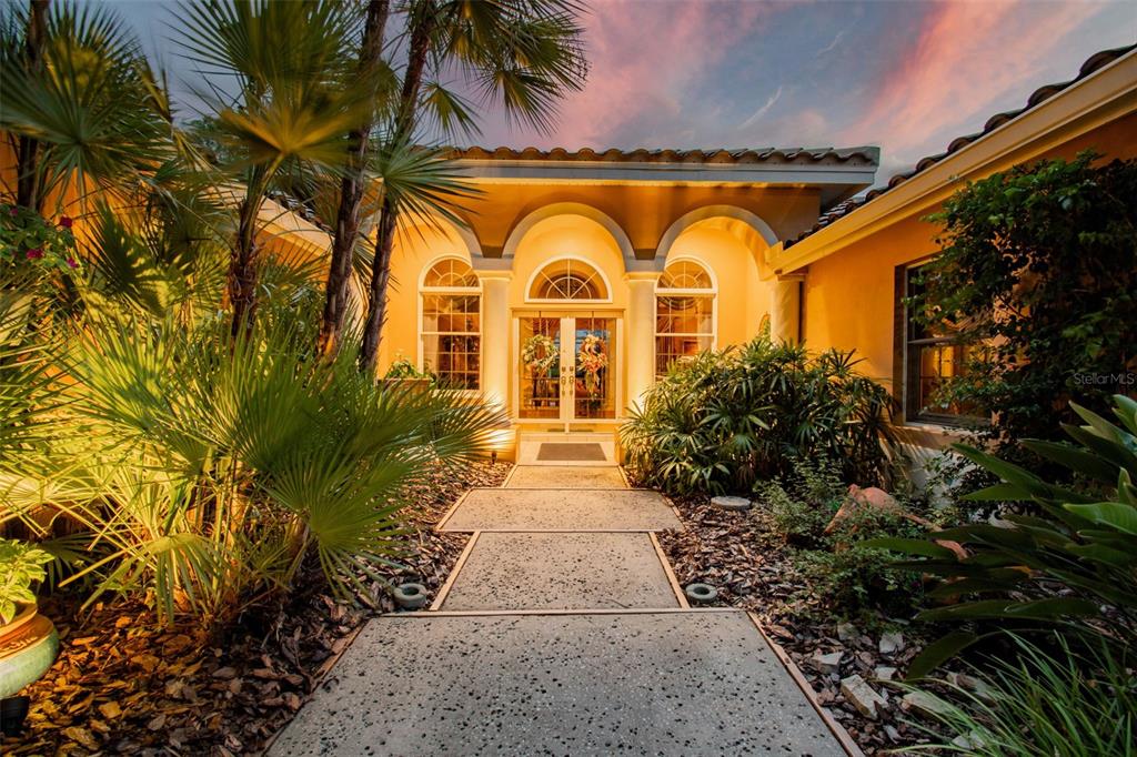 A paved walkway leads to the arched entryway of a house with yellow stucco walls — 17714 GREY EAGLE ROAD, TAMPA, FL