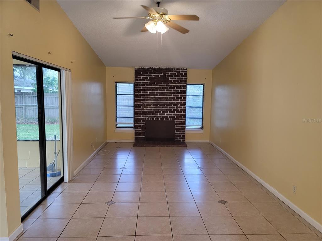 A living room features yellow walls, tile flooring, a brick fireplace, and sliding glass doors — 41 CHIP COURT, KISSIMMEE, FL