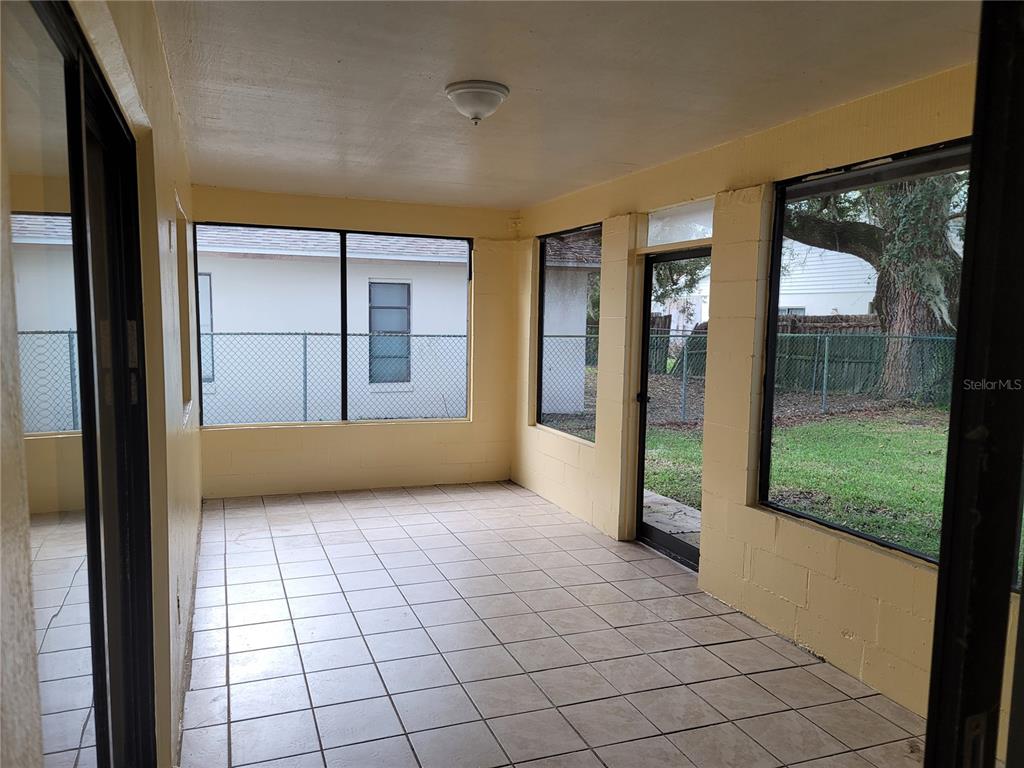 A sunroom features yellow painted block walls, white tiled flooring, and large windows overlooking a yard — 41 CHIP COURT, KISSIMMEE, FL