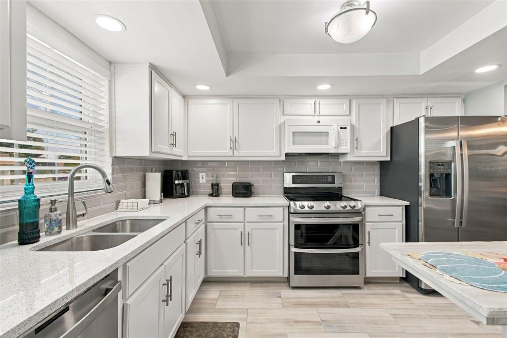 A kitchen with white cabinets and stainless steel appliances opens to a wood-floored living area — 1659 S LAKE AVENUE UNIT 1, CLEARWATER, FL