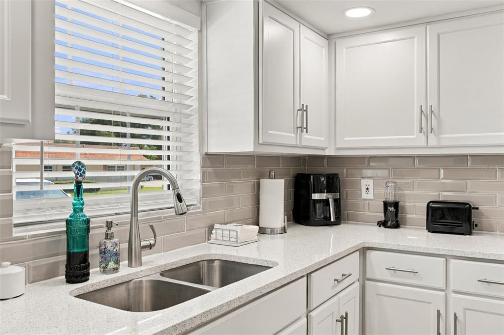 A kitchen features white cabinets, stainless steel appliances, a light-colored backsplash, and a dining area — 1659 S LAKE AVENUE UNIT 1, CLEARWATER, FL