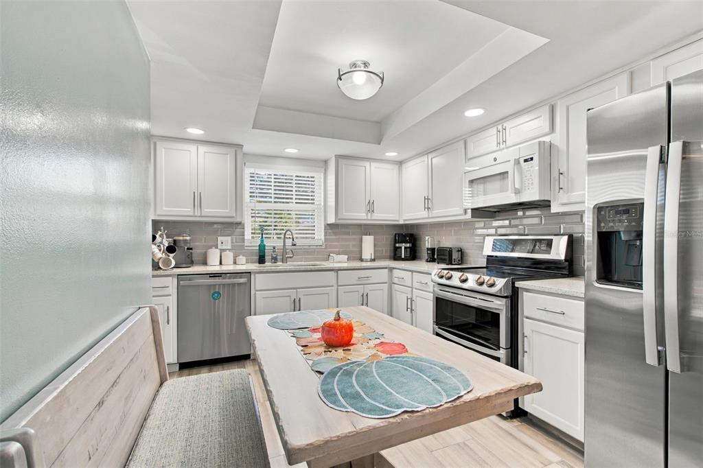 A kitchen features white cabinets, stainless steel appliances, a gray tile backsplash, and a dining table — 1659 S LAKE AVENUE UNIT 1, CLEARWATER, FL