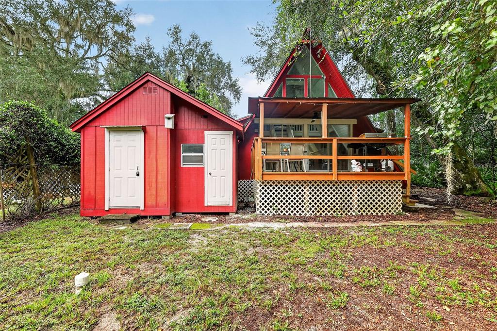 A red cabin with an attached A-frame structure and a wooden deck sits outdoors — 10388 SW 64TH AVENUE, BUSHNELL, FL