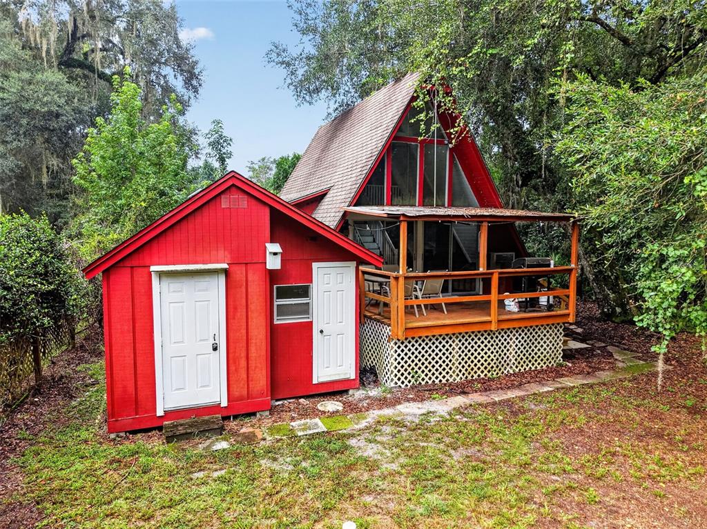 A red A-frame house with an attached shed and a wooden deck sits among trees — 10388 SW 64TH AVENUE, BUSHNELL, FL