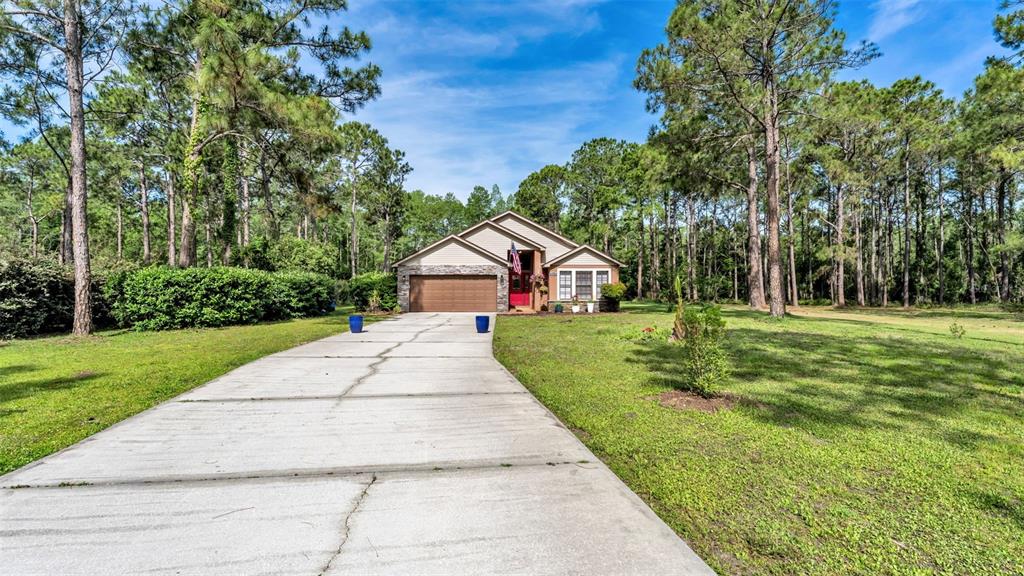 A single-story house with a stone facade and a long concrete driveway sits among trees — 13409 SWEET HILL ROAD, POLK CITY, FL