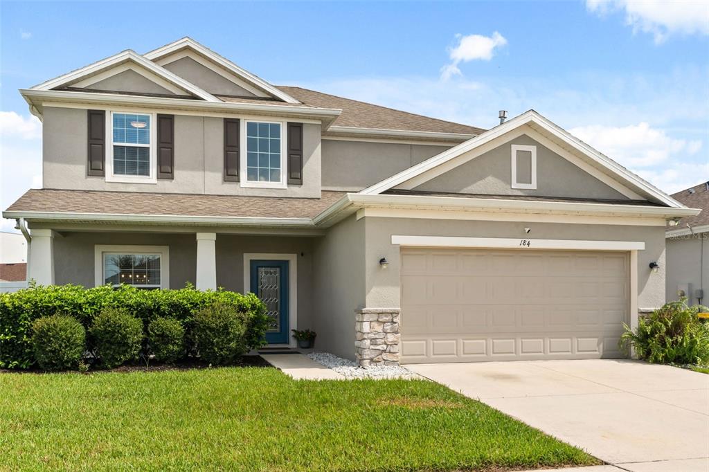 A two-story suburban house features a tan stucco exterior, a two-car garage, and front landscaping — 184 BELLA VERANO WAY, DAVENPORT, FL