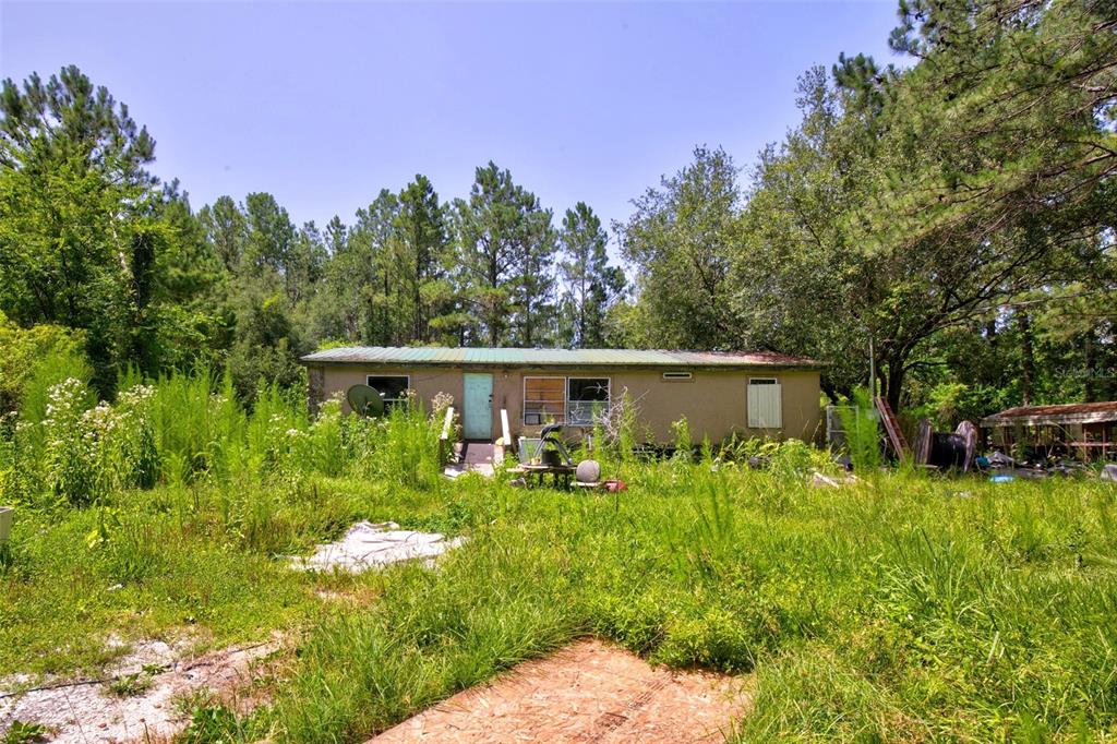 A single-story house with a metal roof sits in a yard with overgrown grass — 7320 NE 137TH PLACE, CITRA, FL
